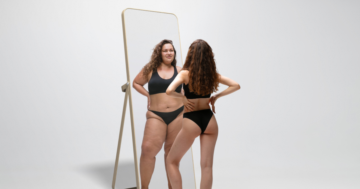 woman wearing bathing suit looking her body at the mirror